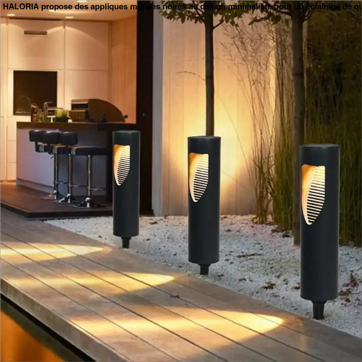 Trois appliques murales noires cylindriques avec une découpe feuille lumineuse ambre pour chemin extérieur