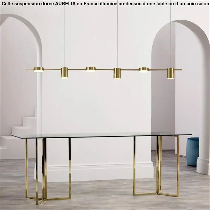 Grande suspension doree aurelia en métal doré avec cinq ampoules cylindriques suspendue au-dessus d’une table en verre