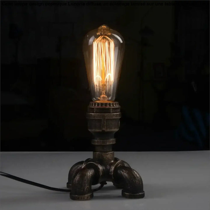 Lampe de table forge en style industriel avec ampoule à filament dans verre transparent sur base métallique sombre pour décoration intérieure chaleureuse