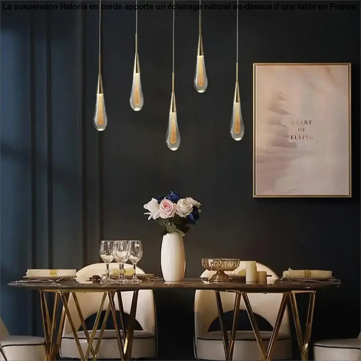 Lampe suspendue corde haloria avec cinq suspensions élégantes en verre clair et métal doré au-dessus d’une table