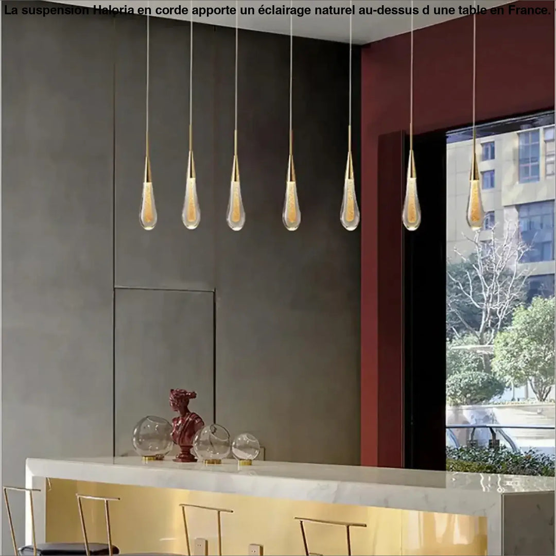 Cinq lampes suspendues corde haloria dorées avec abat-jour en verre en forme de goutte au-dessus d’une table ou d’un coin salon