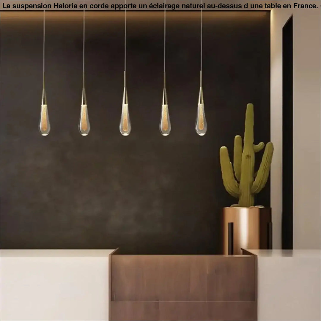 Lampe suspendue corde haloria avec cinq abat-jours en verre clair en forme de goutte suspendues au-dessus d’une table
