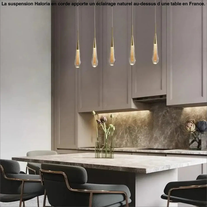 Lampe suspendue corde haloria avec cinq suspensions en verre clair et métal doré au-dessus d’une table de cuisine