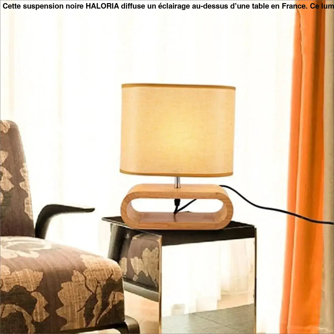 Lampe suspendue noir avec abat-jour cylindrique ton chaud sur base en bois clair courbée au-dessus d’une table