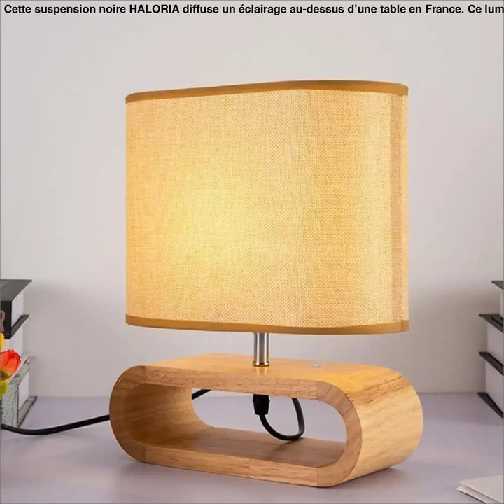 Lampe suspendue noir avec abat-jour beige en tissu texturé et base en bois clair au-dessus d’une table ou d’un coin salon