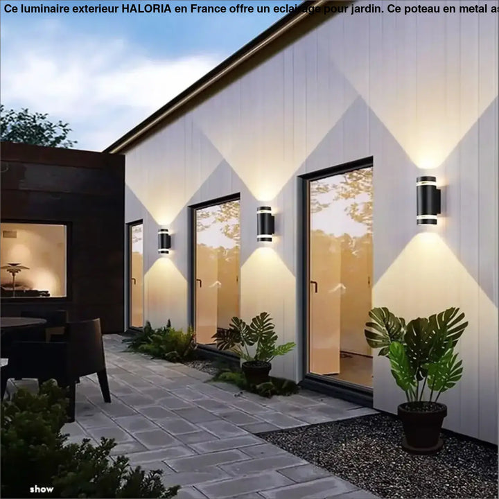 Poteau pour luminaire exterieur haloria avec appliques murales noires cylindriques et accents metalliques côté d’un canapé