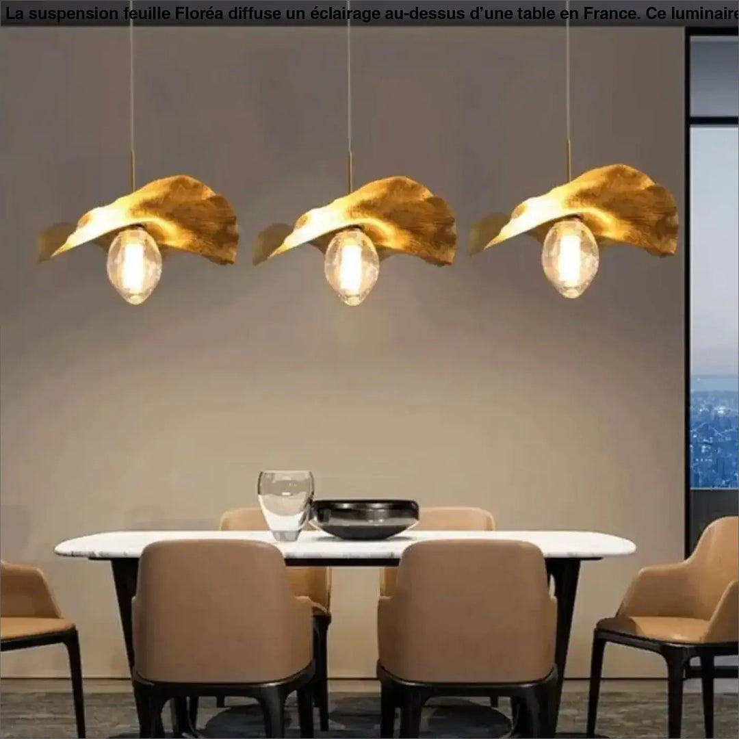 Suspension feuille floréa avec trois luminaires dorés en forme de feuille au-dessus d’une table ou d’un coin salon