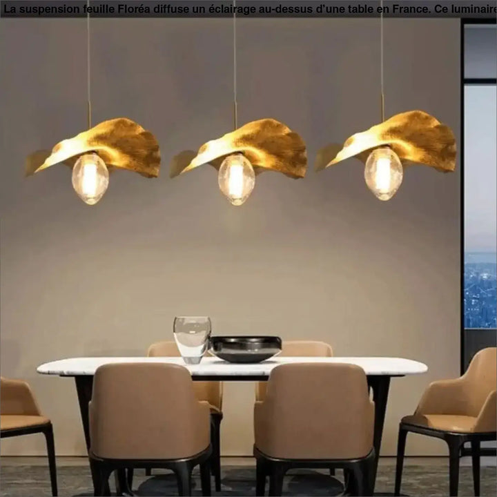 Suspension feuille floréa avec trois luminaires dorés en forme de feuille au-dessus d’une table ou d’un coin salon
