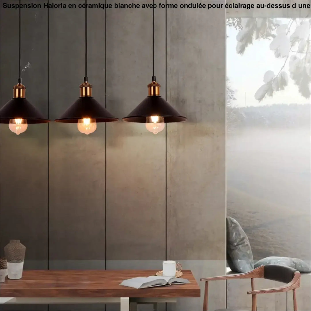 Trois suspensions luminaire ceramique blanc à forme ondulée avec accents en laiton suspendues au-dessus d’une table en bois
