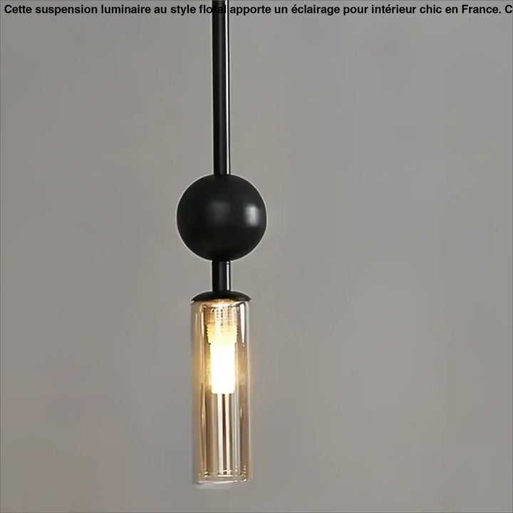 Suspension luminaire krysta avec boule métallique noire et cylindre en verre clair abritant une ampoule éclairée