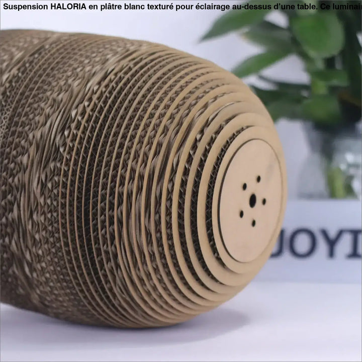 Suspension luminaire moderne en platre texture blanc installée au-dessus d’une table avec un griffoir en carton beige au coin salon