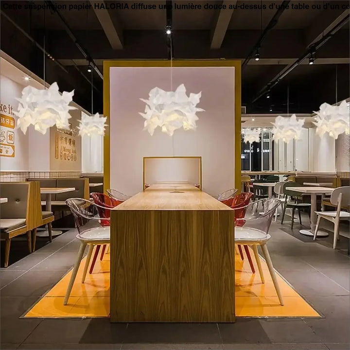 Longue table à manger en bois clair avec finition grain de bois au-dessus d’une table suspension papier haloria
