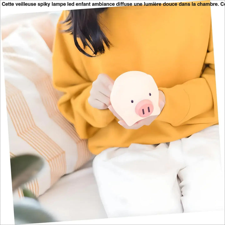 Veilleuse spiky lampe led enfant tenue délicatement avec une peluche cochon blanc au museau rose